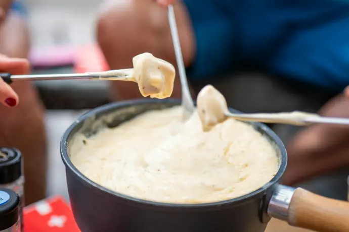 People dipping bread into a pot of cheese fondue
